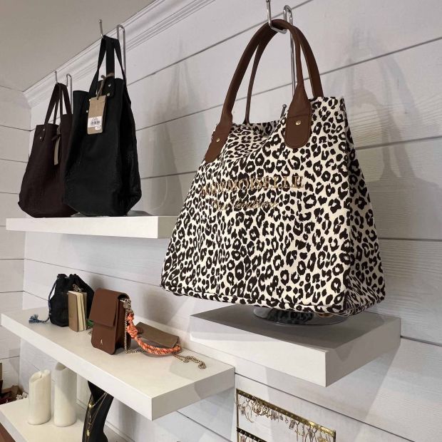 Sac imprimé léopard avec anses en cuir, exposé avec d'autres modèles de maroquinerie chez Moi d'Abord à Divonne-les-Bains.